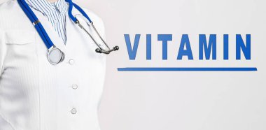 Beyaz arka planda Kelime Vitamini. Yakınlarda beyaz önlüklü ve steteskoplu bir doktor var. Tıbbi konsept