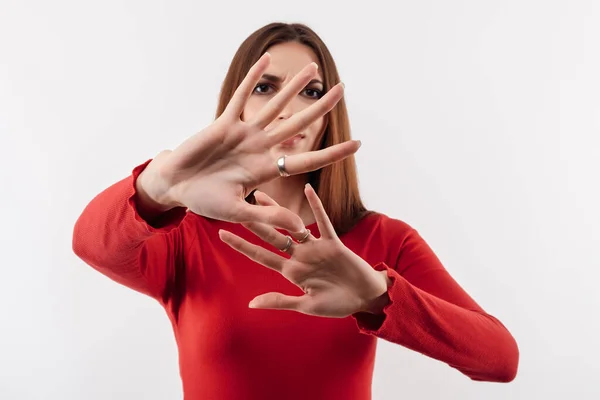 No way, stop doing. Image of dissatisfied girl with long chestnut hair in casual red sweater doing disgust face because aversion reaction with hands raised. Studio shot, white background