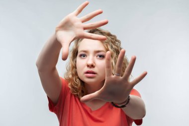 Kıvırcık saçlı, sıradan tişörtlü ciddi sarışın bir kızın görüntüsü aktif olarak kameraya el hareketi yapıyor, elleriyle hareket etmeyi kes. Olmaz, kes şunu. Stüdyo fotoğrafı, beyaz arka plan. İnsan duyguları kavramı