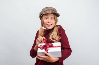 12-15 yaşlarında sıradan bir kazak giymiş, elinde kurdeleyle süslenmiş bir hediye taşıyan mutlu bir sarışın kızın portresi. Stüdyo beyaz arka plan çekti, izole. Yeni Yıl, Kadınlar Günü, Doğum günü, Tatil konsepti