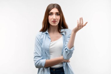 Uzun kestane rengi saçlı, sıradan giyinmiş, omuz silkmiş, avuçlarını kaldırarak hareket eden ve soruyla kafası karışmış bir kızın stüdyo fotoğrafı. İnsan duyguları kavramı