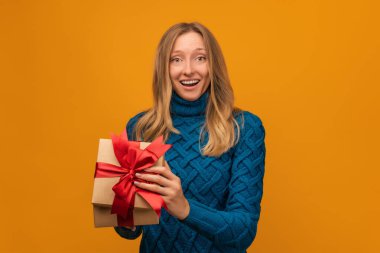 Kurdeleyle süslenmiş çekici genç bir kadın sarı arka planda şaşırmış yüz ifadesiyle poz veriyor. Yeni Yıl, Kadınlar Günü, Doğum günü, Tatil konsepti