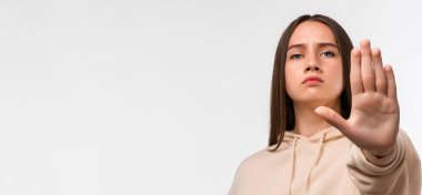 Uzun kestane rengi saçları olan, ciddi ve sert görünen, sıradan bej kapüşonlu giyinen, avuçlarını açık bırakan genç, güzel bir kadın. Metnin için boşluk kopyala