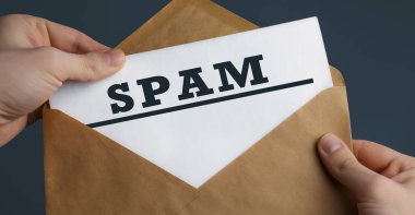 Mavi arka planda kelime spam, iletişim konsepti içeren el sanatları zarfı tutan bir erkeğin yakın çekimi