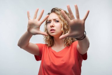 Kıvırcık saçlı, sıradan tişörtlü ciddi sarışın bir kızın görüntüsü aktif olarak kameraya el hareketi yapıyor, elleriyle hareket etmeyi kes. Olmaz, kes şunu. Stüdyo fotoğrafı, beyaz arka plan. İnsan duyguları kavramı