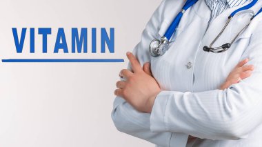 Beyaz arka planda Kelime Vitamini. Yakınlarda beyaz önlüklü ve steteskoplu bir doktor var. Tıbbi konsept