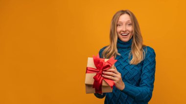 Kurdeleyle süslenmiş çekici genç bir kadın sarı arka planda şaşırmış yüz ifadesiyle poz veriyor. Yeni Yıl, Kadınlar Günü, Doğum günü, Tatil konsepti