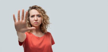 Kıvırcık saçlı, sıradan tişörtlü, elinde avuç içi ile dur işareti yapan ciddi sarışın bir kız resmi. Yüzünde uyarı ifadesi var. Stüdyo fotoğrafı, beyaz arka plan. İnsan duyguları kavramı