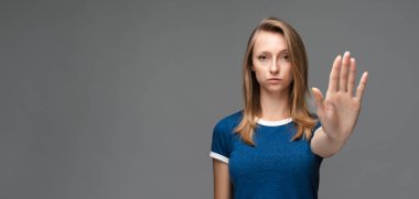 Mavi tişörtlü, sarı düz saçlı, ciddi bir kız eli ile durduğunu gösteriyor, işaret ediyor, reddedildiğini gösteriyor, şiddete, vücut diline izin vermiyor. Metnin için boşluk kopyala