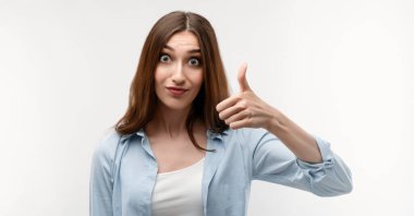 Uzun kestane rengi saçları olan beyaz bir kadın, günlük giysiler giymiş, iki eliyle işaret ediyor, onaylıyor, beyaz arka planda izole edilmiş..