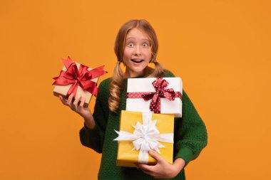 12-14 yaşlarında, elinde bir sürü hediye kutusu olan yeşil kazaklı çekici bir kız resmi. Stüdyo fotoğrafı, sarı arka plan, izole edilmiş. Yeni Yıl Kadınların Doğum Günü Tatil Konsepti