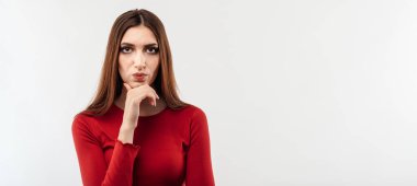 Uzun kestane rengi saçlı, düşünceli, kameraya bakan kırmızı süveter giyen hoş bir kadın resmi. İnsani duygular, yüz ifadesi kavramı. Stüdyo çekimi, beyaz arkaplan