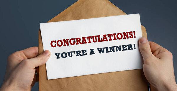 Male hands holding craft envelope with text CONGRATULATIONS YOU'RE A WINNER on blue background, communication concept