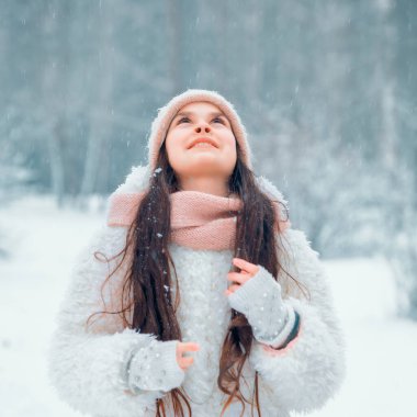 10-12 yaşlarında güzel bir kız kış ormanında yürüyor. Sıcak beyaz kışlık kıyafetler, Noel havası. Seçici odak, ton ve gürültüye sahip resim