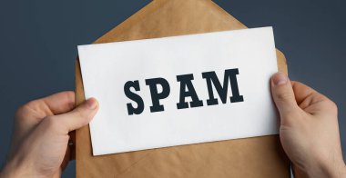 Male hands holding craft envelope with word SPAM on blue background, communication concept