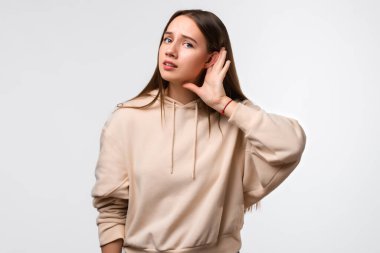 Genç, güzel esmer kadın, elini kulağına yakın tutuyor. Sanki beyaz arka plandaki dedikoduları dinliyormuş gibi.