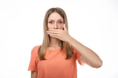 Gayri resmi giyinmiş, hayal kırıklığına uğramış sarışın kız önemli bir şeyi açıklamamak için ağzını eliyle kapatıyor. Sır tut. Stüdyo çekimi, beyaz arkaplan