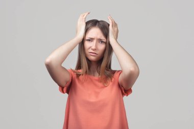 Endişeli, endişeli ve endişeli sarışın kızın portresi, başını tutup panikleyen, panikleyen, korkmuş ve gergin hisseden, ne yaptığını bilmeyen. Stüdyo çekimi, gri arkaplan