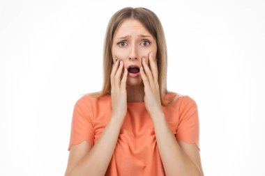 Endişeli ve endişeli, sıradan giysili sarışın kız korkmuş bir ifadeyle bakıyor. Stüdyo çekimi, beyaz arkaplan