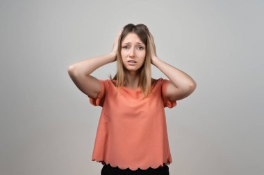 Endişeli, endişeli ve endişeli sarışın kızın portresi, başını tutup panikleyen, panikleyen, korkmuş ve gergin hisseden, ne yaptığını bilmeyen. Stüdyo çekimi, gri arkaplan