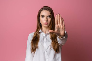 Uzak dur ve beni rahat bırak. Ciddi esmer kız avuç içini kameraya çekiyor, yasaklama işareti yapıyor, yasaklıyor ya da uyarıyor, dur işaretinde kolunu uzatıyor. Stüdyo çekimi, pembe arkaplan