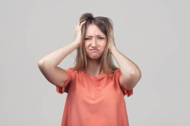 Panik içinde genç sarışın bir kadının korku ve hayal kırıklığı içinde başını tutuşu. Stres ve akıl sağlığı. Stüdyo çekimi, gri arkaplan