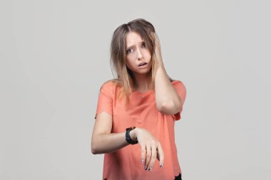 Çok geç, acele et. Sarışın, güzel bir kadın kol saatine bakıyor, sabırsız, gecikme yüzünden üzgün ve kızgın. Stüdyo çekimi, gri arkaplan