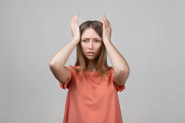 Endişeli, endişeli ve endişeli sarışın kızın portresi, başını tutup panikleyen, panikleyen, korkmuş ve gergin hisseden, ne yaptığını bilmeyen. Stüdyo çekimi, gri arkaplan