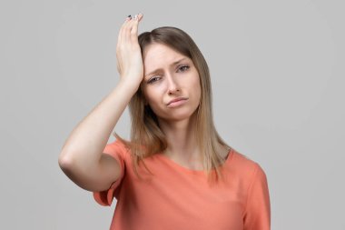 Endişeli, hayal kırıklığına uğramış, yorgun hisseden genç sarışın kız, baş ağrısı, baş ağrısı ya da migren ağrısı gibi. Stüdyo çekimi, gri arkaplan