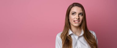 Düşünceli, çekici, esmer, dudak ısıran bir kızın fotoğrafı. Stüdyo fotoğrafı, pembe arka plan. Kopyalama alanı oluştur