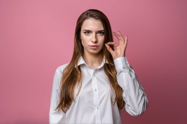 Sırların benim konseptimle güvende. Esmer kız, gündelik kıyafetleriyle fermuarlı jest yapıyor. Sanki anahtarla ağzını kapatıyor gibi. Stüdyo fotoğrafı, pembe arka plan. Sır tut.