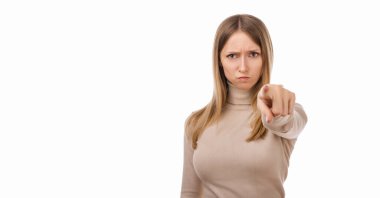 Senin hatandı. Hoşnut olmayan, sıradan elbiseli genç sarışın kadın kamerayı sana doğrultuyor, kızgın ve öfkeli. Stüdyo fotoğrafı, beyaz arka plan. İlan için yer