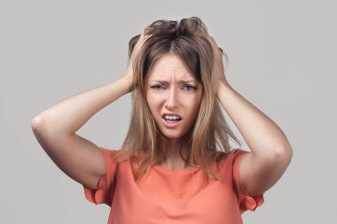 Endişeli, endişeli ve endişeli sarışın kızın portresi, başını tutup panikleyen, panikleyen, korkmuş ve gergin hisseden, ne yaptığını bilmeyen. Stüdyo çekimi, gri arkaplan