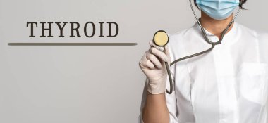 THYROID - gri arkaplanda metin kavramı. Yakınlarda beyaz önlüklü ve steteskoplu bir doktor var. Tıbbi konsept