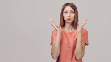 Endişeli ve endişeli sarışın kız şaşırmış bir ifadeyle bakıyor, nasıl davrandığı hakkında hiçbir fikri yok, utanmış ve endişeli. Stüdyo çekimi, gri arkaplan