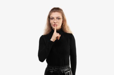 Genç, sıska bir kadın ciddi görünüyor ve parmaklarını dudaklarına bastırıp sessizlik ya da sessizlik talep ediyor, sır saklıyor. Sessizlik ve gizli konsept. Stüdyo çekimi, beyaz arkaplan, izole edilmiş