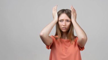 Endişeli, endişeli ve endişeli sarışın kızın portresi, başını tutup panikleyen, panikleyen, korkmuş ve gergin hisseden, ne yaptığını bilmeyen. Stüdyo çekimi, gri arkaplan