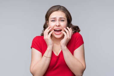 Şok olmuş, ağzı açık, el hareketi yapan, gri arka planda duran korkmuş bir kadının portresi. İnsani duygular, yüz ifadesi kavramı