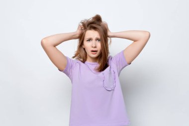 Panik içinde, korku ya da hüsran içinde başını tutan sıradan tişörtlü bir kızın portresi. Stres ve akıl sağlığı. Stüdyo çekimi, beyaz arkaplan