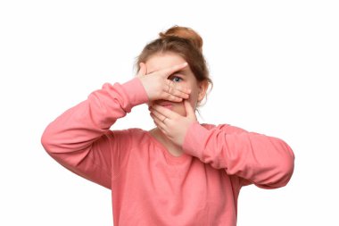 Korkmuş genç kız yüzünü avuç içlerine gizliyor ve bir gözü parmaklarının arasında dışarı bakıyor, korkudan titriyor, ürkütücü sesten çok korkuyor, beyaz arka planda izole edilmiş.