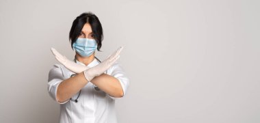 Koruyucu yüz maskesi takan ciddi kadın doktor ya da bilim adamı iki kolu çapraz tutuyor, duruyor ya da jesti yasaklıyor. Koru kendini. Tıp ve sağlık hizmetleri kavramı. İlan için yer