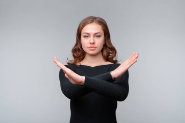 Dur işareti, sembol - kıpırdama. Ciddi bir esmer kadın kameraya bakarken dur hareketi yapıyor. Stüdyo çekimi, gri arkaplan