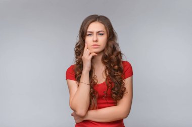 Hmm, ilginç. Düşünceli genç esmer kadın, kameraya bakıyor ve bir şeyler düşünüyor, varsayımda bulunuyor, düşünüyor. Stüdyo fotoğrafı, gri arka plan. İnsani duygular, yüz ifadesi kavramı