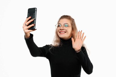 Akıllı telefon aracılığıyla video iletişimi. Genç bir kadın video görüşmesi için telefon kullanıyor, online görüşme, beyaz arka planda duruyor. Arkadaşlarıyla konuşuyor.