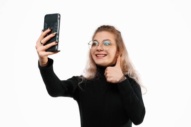 Akıllı telefon aracılığıyla video iletişimi. Genç bir kadın video görüşmesi için telefon kullanıyor, online görüşme, beyaz arka planda duruyor. Arkadaşlarıyla konuşuyor.