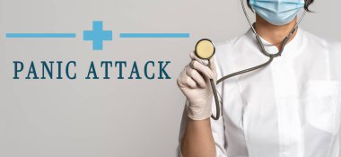 PANIC ATTACK - gri arkaplan üzerine metin konsepti. Yakınlarda beyaz önlüklü doktor, koruyucu yüz maskesi ve stetoskop var. Tıbbi konsept