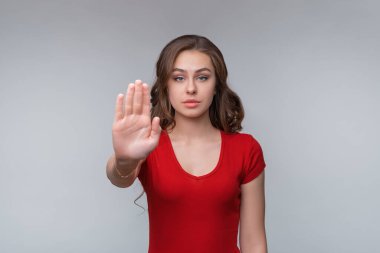 Dur işareti, kamerada avuç içi, sembol - kıpırdama. Ciddi genç esmer kadın avucunu kameraya gösteriyor. Stüdyo çekimi, gri arkaplan