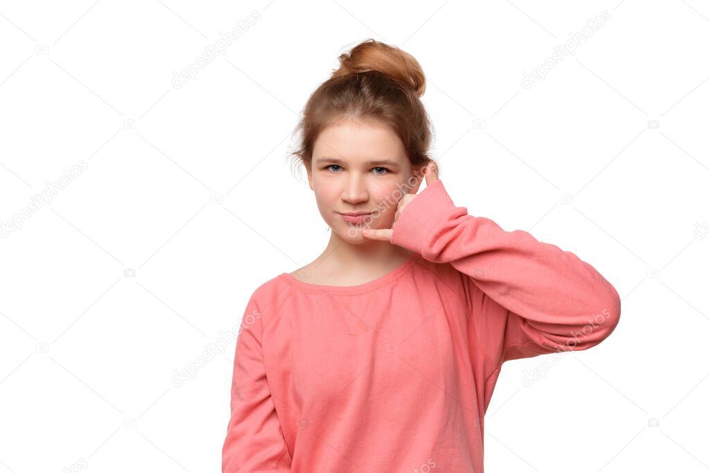 teen girl imitates telephone conversation, keeps hand near ear as if holding mobile phone, saying call me. Body language concept. Studio shot, white background