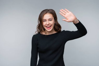 Selam, naber? Dost canlısı genç esmer kadının portresi gülümseyen ve selamlayan, merhaba demek için el sallayan, selamlayan arkadaşlar, merhaba deyin ve hoş geldiniz, elveda jesti, gri arka planda duran