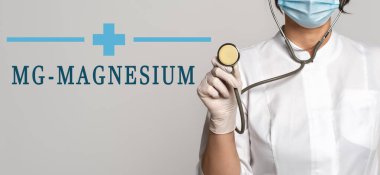 MAGNESIUM - gri arkaplanda metin kavramı. Yakınlarda beyaz önlüklü doktor, koruyucu yüz maskesi ve stetoskop var. Tıbbi konsept